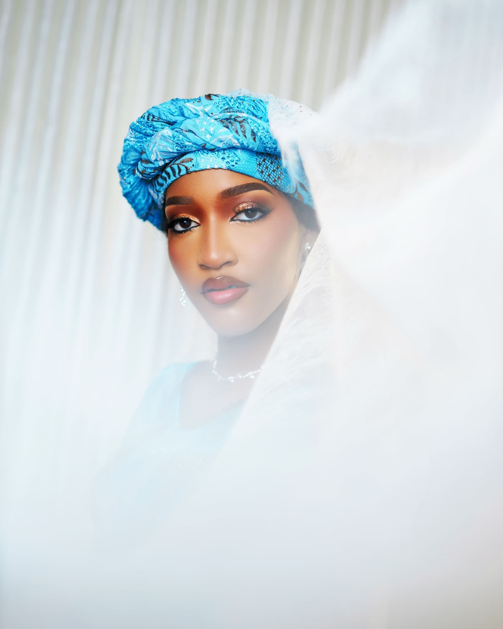 Close portrait in a blue gele behind a sheer white veil