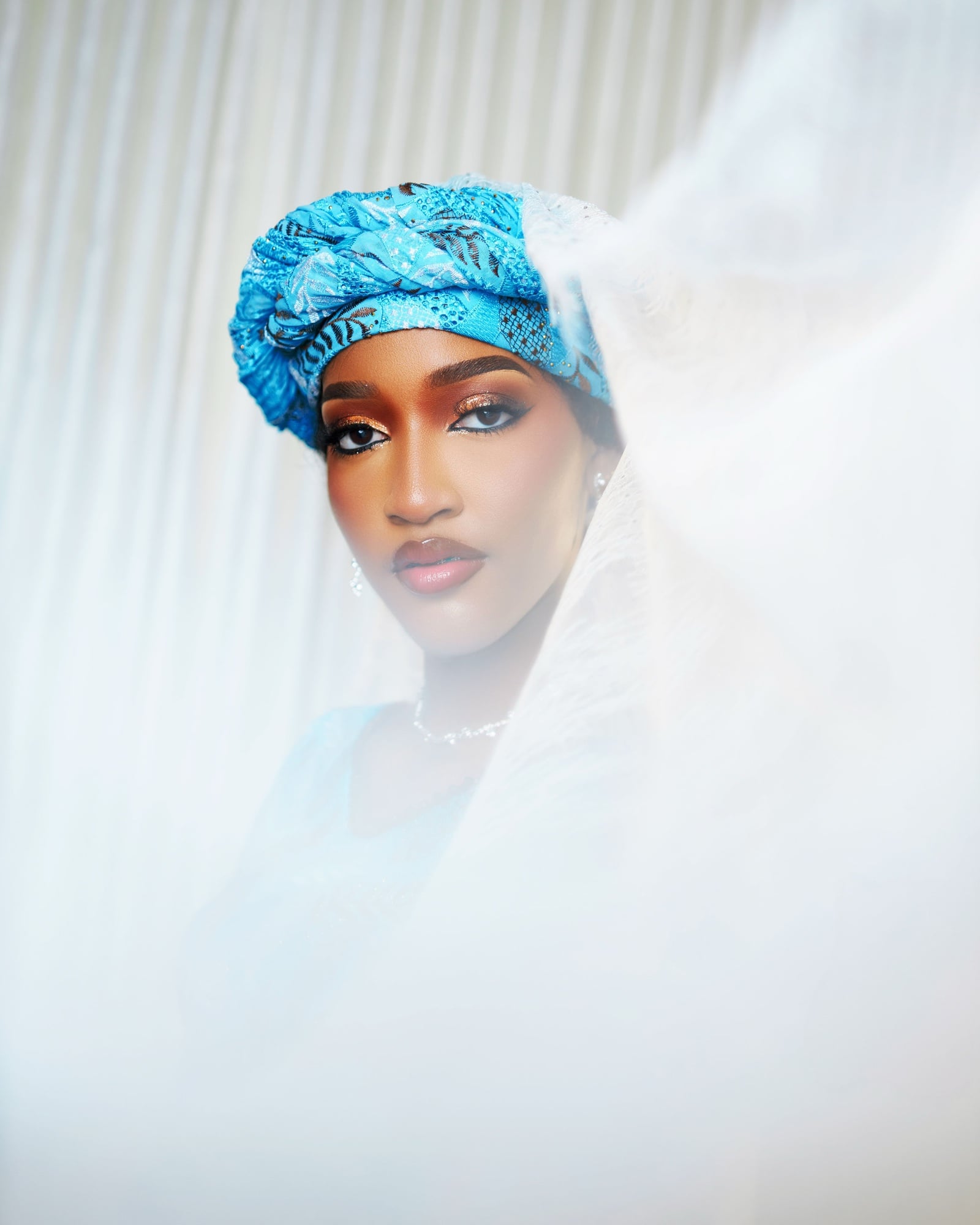 Bluethopia in a blue gele, framed by a sheer white veil